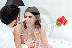 Couple drinking sparkling wine on bed.