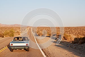 Couple driving convertible car on desert highway, back view