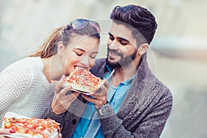 Couple eating pizza outdoors and smiling.