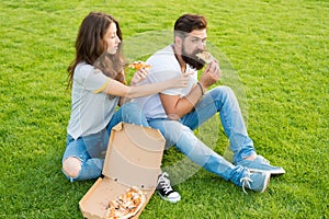 Couple eating pizza relaxing on green lawn. Fast food delivery. Bearded man and woman enjoy cheesy pizza. Couple in love