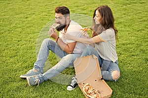 Couple eating pizza relaxing on green lawn. Fast food delivery. Bearded man and woman enjoy cheesy pizza. Couple in love