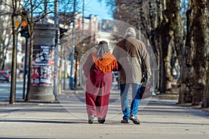 A couple of eldery people in hands are walking through the city street. Rear view