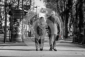 A couple of eldery people in hands are walking through the city street. Rear view