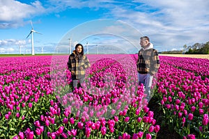 A couple embraces in a vast field of vibrant purple tulips, under the watchful gaze of towering windmill turbines in the