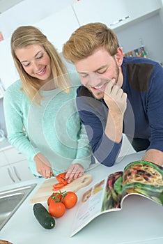 Couple embracing in kitchen while checking recipe book