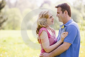 Couple embracing outdoors holding flower smiling