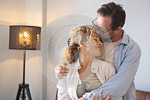 Couple embracing and romancing standing in living room at home. Husband kissing forehead of wife with affection. Affectionate