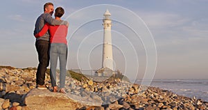 Couple embracing by the sea near a lighthouse
