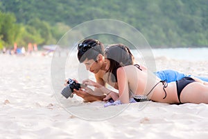 Couple enjoy and happy fun on beach laughing together looking at summer vacation travel photo pictures on retro vintage camera. Ho