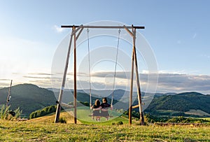 Couple enjoying the joys of being on an outdoor wooden swing during summer sunset.