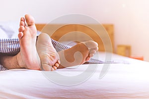 Couple is enjoying the morning in bed: Close up of uncovered feet in the bed, blanket