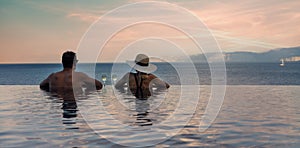 Couple enjoying romantic view to the sea and drinking champagne in infinity pool at luxury resort. banner copy space