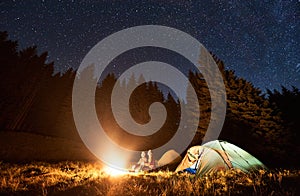 Couple enjoying starry night sky near campfire.
