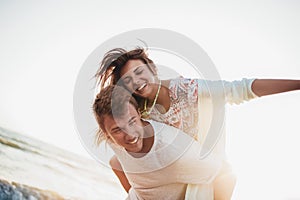 Couple enjoying summer holidays. Handsome young man giving piggyback ride to girlfriend on beach