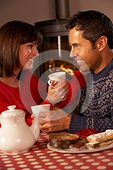 Couple Enjoying Tea And Cake By Cosy Log Fire