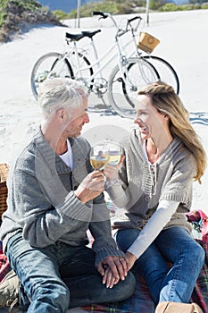 Couple enjoying white wine on picnic at the beach smiling at each other