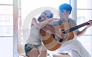 Couple entertainment concept. Young man playing guitar for his girlfriend listening at home together