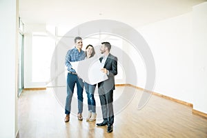 Couple And Estate Agent Discussing Over Blueprint In New Apartment