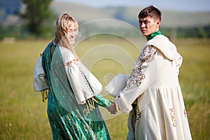 Couple in ethnic costumes hold hands turned back to camera.