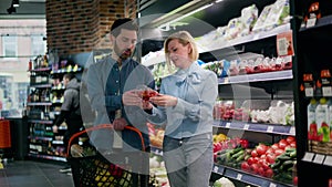 Couple examining product in produce section near shelves stocked with fruits
