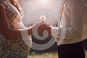 Couple expecting a child holding hands with rose flower facing each other.