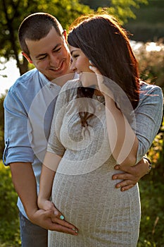 Couple family in the expectation of a baby hugging in sun rays