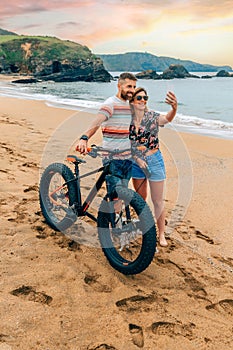 Couple with fat bike taking a selfie with the mobile on the beach