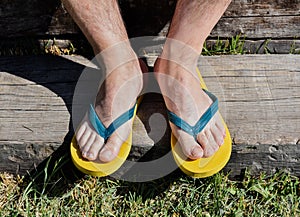 a couple of feet completely barefoot wearing two yellow and blue flip flops on a wooden step. The man is resting in the garden in