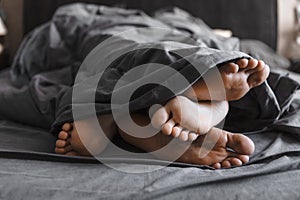 couple feet under the blanket in bed with grey sheets