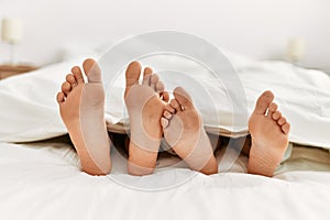 Couple feet under sheets on the bed at home