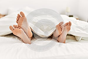 Couple feet under sheets on the bed at home