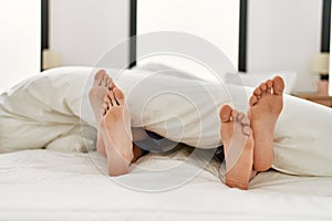 Couple feet under sheets on the bed at home