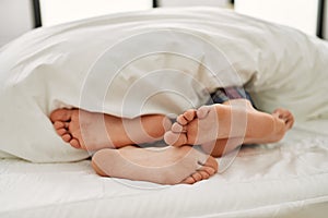 Couple feet under sheets on the bed at home