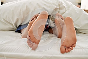 Couple feet under sheets on the bed at home