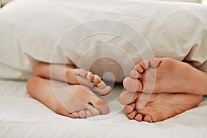 Couple feet under sheets on the bed at home