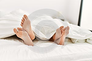 Couple feet under sheets on the bed at home