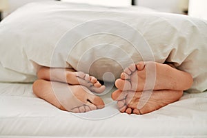 Couple feet under sheets on the bed at home