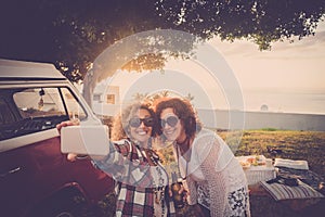 Couple of female friends enjoy and have fun together taking selfie in outdoor - vintage red van and sunlight in background -