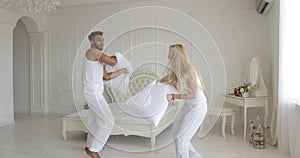 Couple fighting pillows bedroom mix race man woman playing having fun together