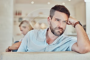 Couple fighting, sitting apart on the couch. Caucasian man looking upset with his wife. Depressed couple ignoring each