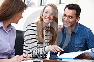 Couple With Financial Advisor Signing Document In Office