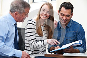 Couple With Financial Advisor Studying Document In Office