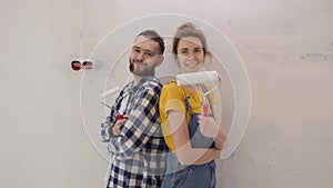 Couple finished repair works painting wall together and standing back to back with tools