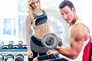 Couple in fitness gym with dumbbells lifting weight