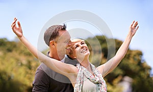 Couple, freedom and smile with love outdoors for honeymoon vacation, together and arms up for happiness. Man, woman and