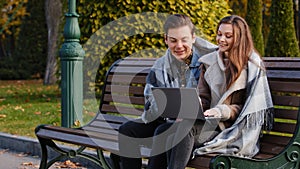 Couple freelancers two partners people young caucasian woman and man entrepreneurs sit on bench in park use urban wifi