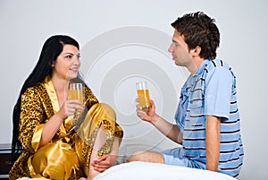 Couple with fresh orange juice on bed in morning