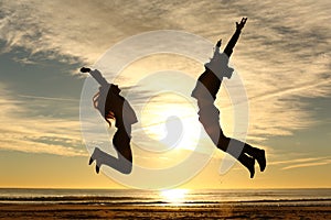 Couple or friends jumping on the beach at sunset