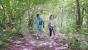 couple of friends walking in nature, african man and hispanic woman hiking in forest in summer