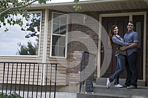 Couple in front of new home holding sold blackboard sign